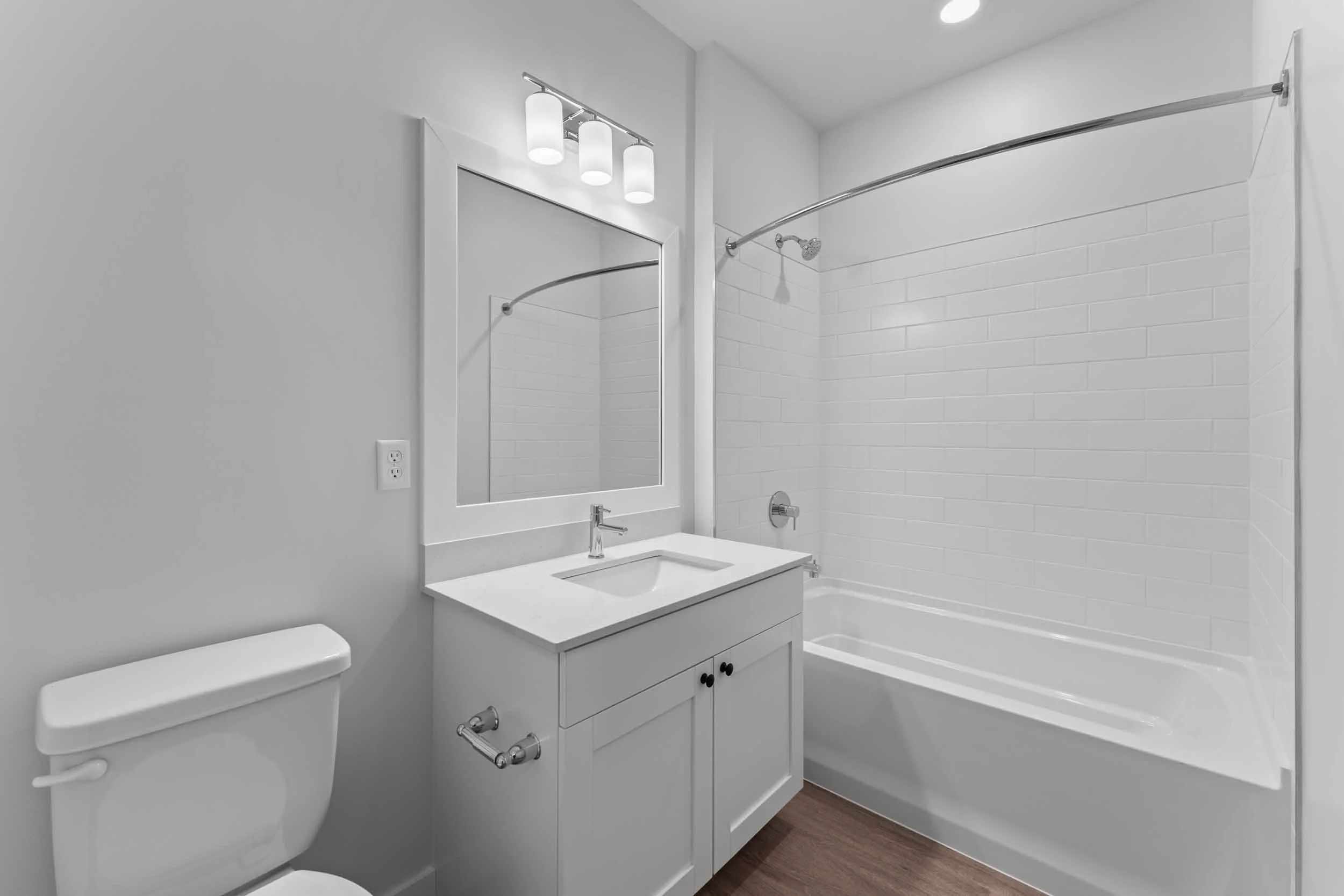 Modern bathroom with white vanity, mirror, light fixture, bathtub, and white tiled walls.