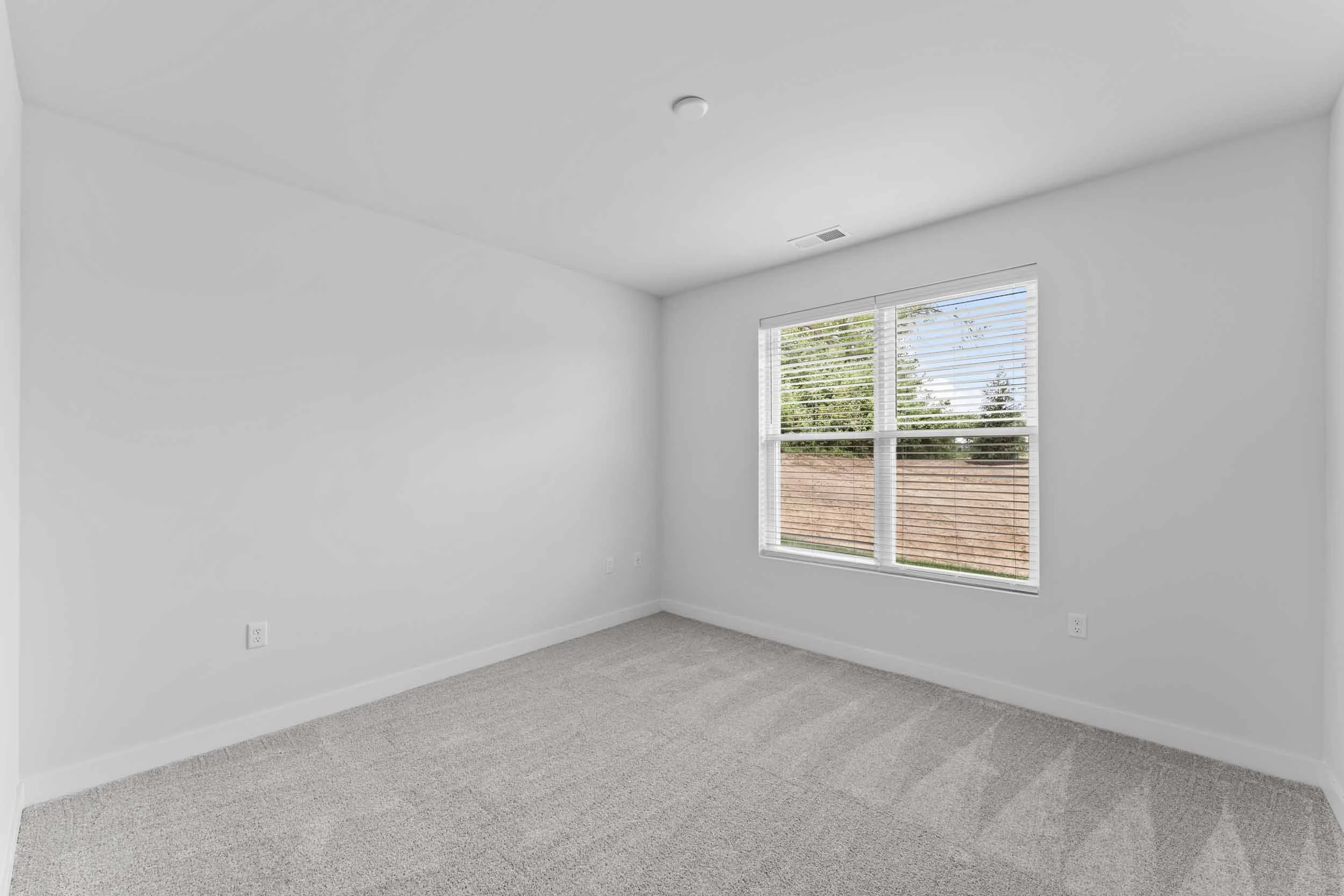 Empty white room with a window, beige carpet, and a ceiling vent.