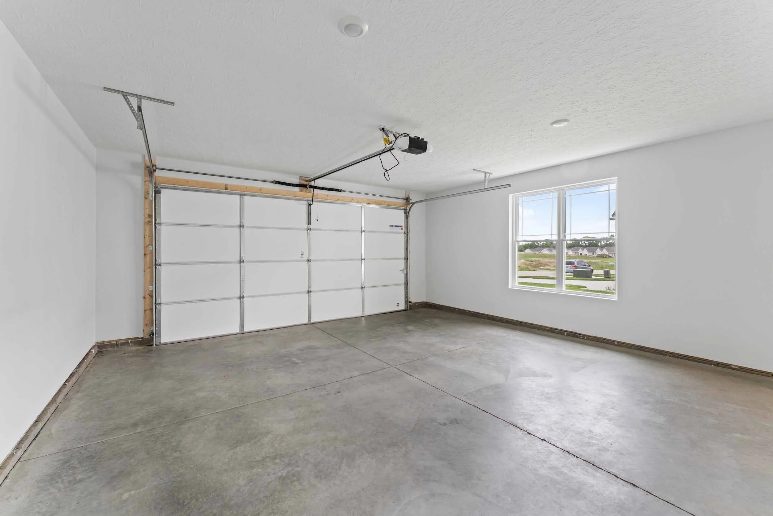 Empty garage with concrete floor, white walls, a large window, and a garage door with an automated opener.