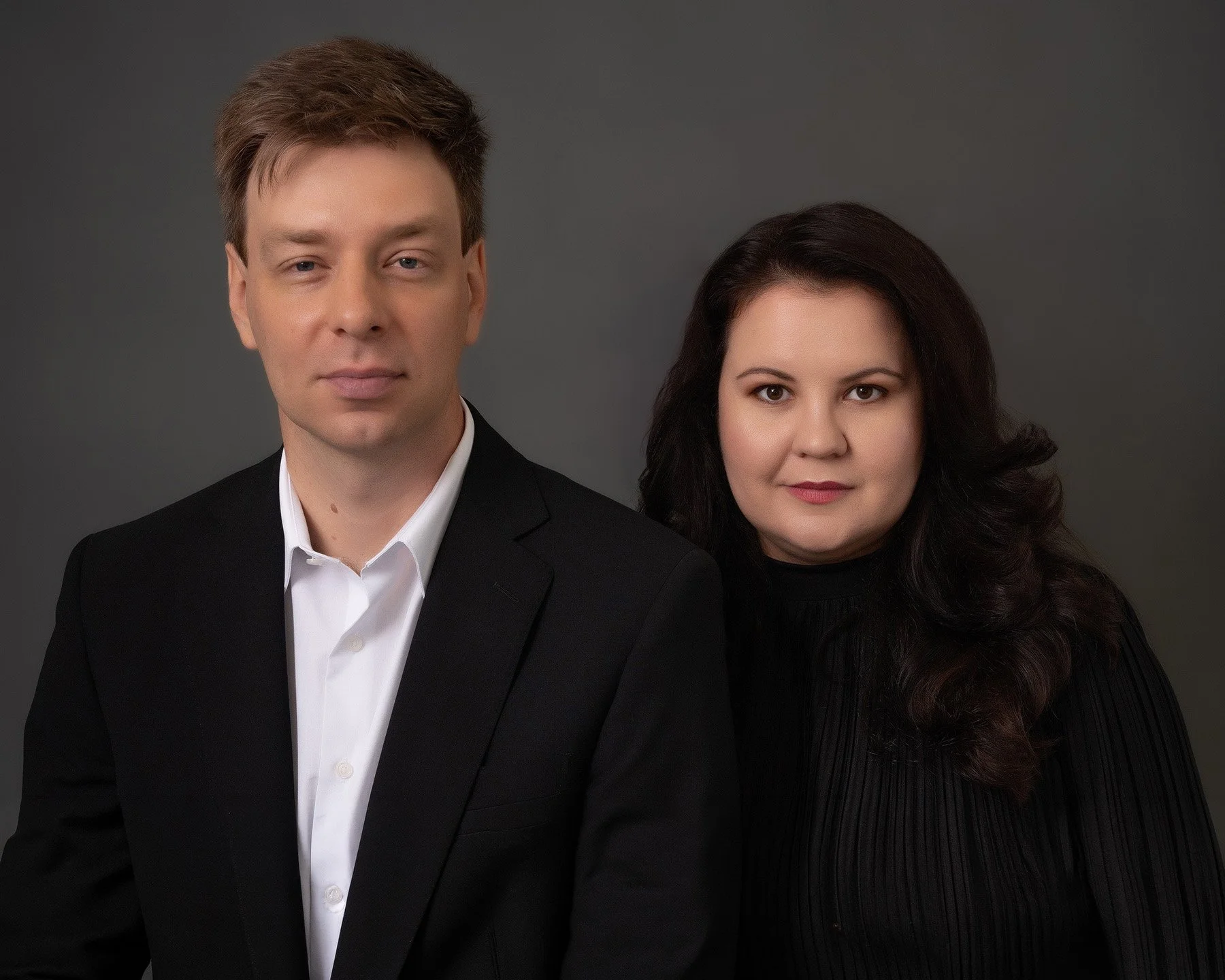 A studio portrait of the classical piano duo Skobin Duo (Sergei Skobin and Diana Skobina) against a dark grey background.