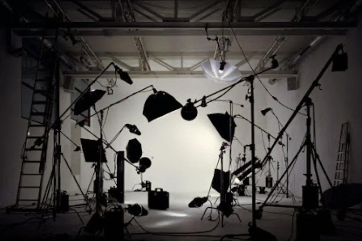 A photography studio with professional lighting equipment, umbrellas, and stands arranged around a white backdrop.