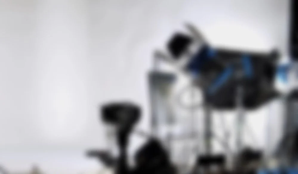 Blurry image of photography or film studio equipment, including lights and stands.