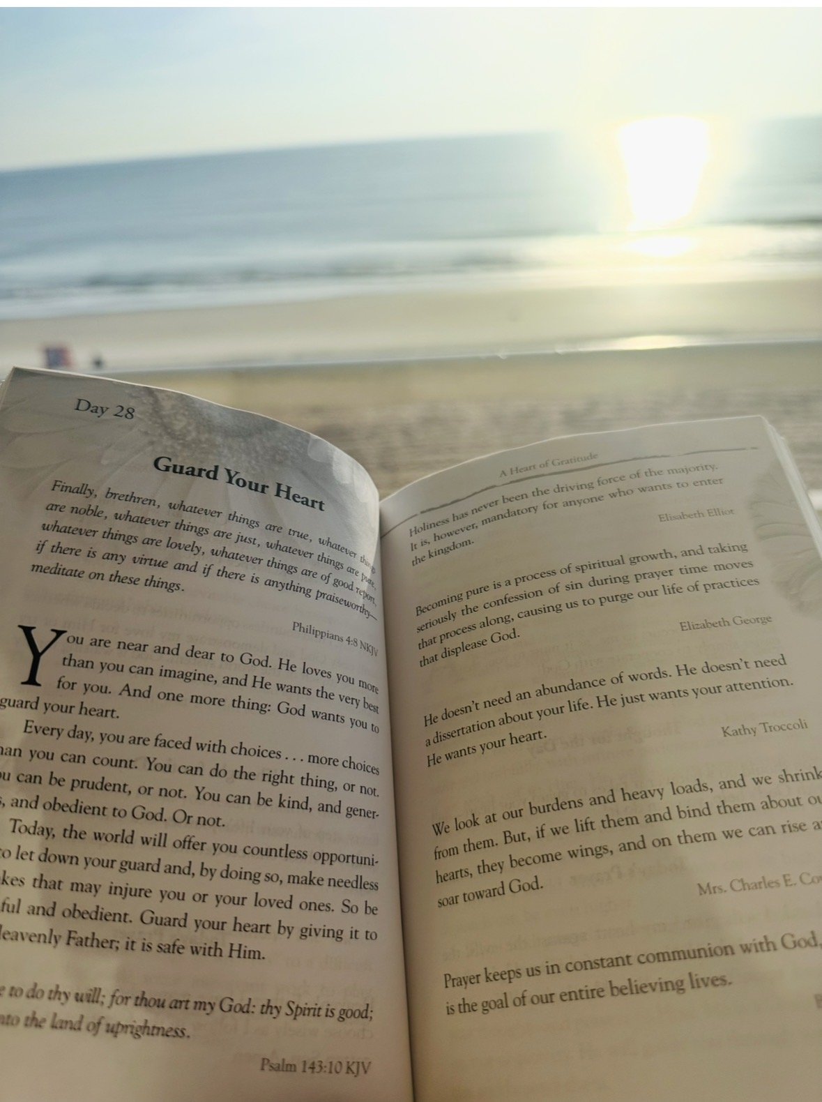 Open Bible on a sandy beach with the ocean and setting sun in the background.