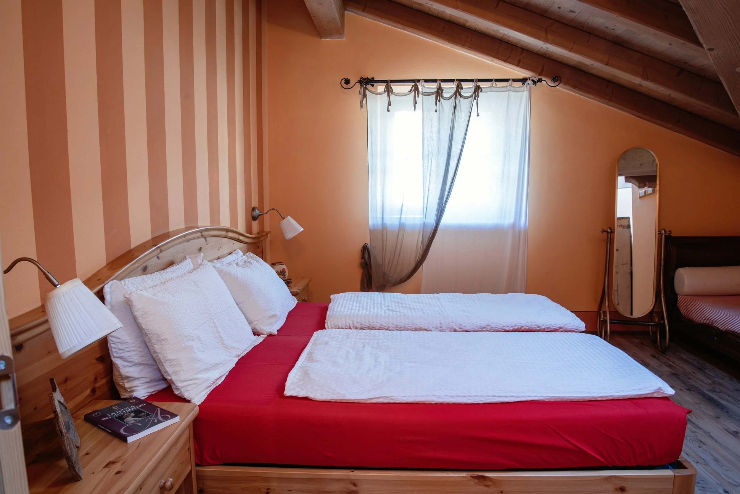 Stanza da letto con letto matrimoniale con cuscini bianchi, copriletto bianco, pareti color pesca e una finestra con tendina semi trasparente