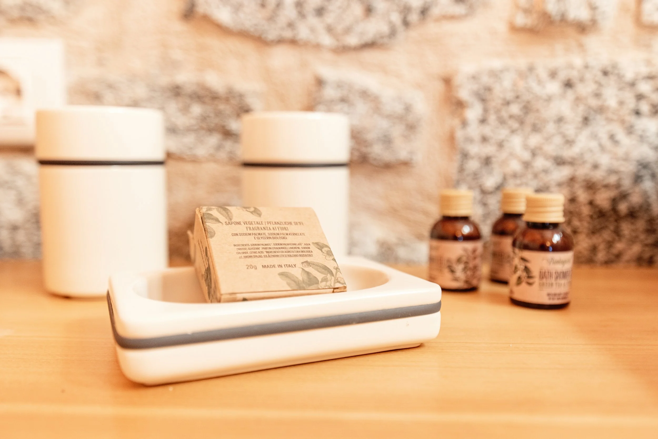 Prodotti per l'igiene personale su un tavolo di legno, tra cui sapone vegetale, crema per le mani e oli essenziali con etichette vintage.