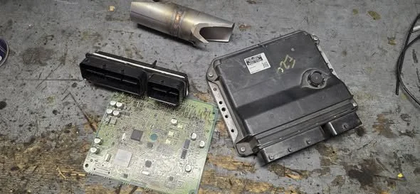 Open electronic control module, circuit board, and cylindrical metal part on a workbench