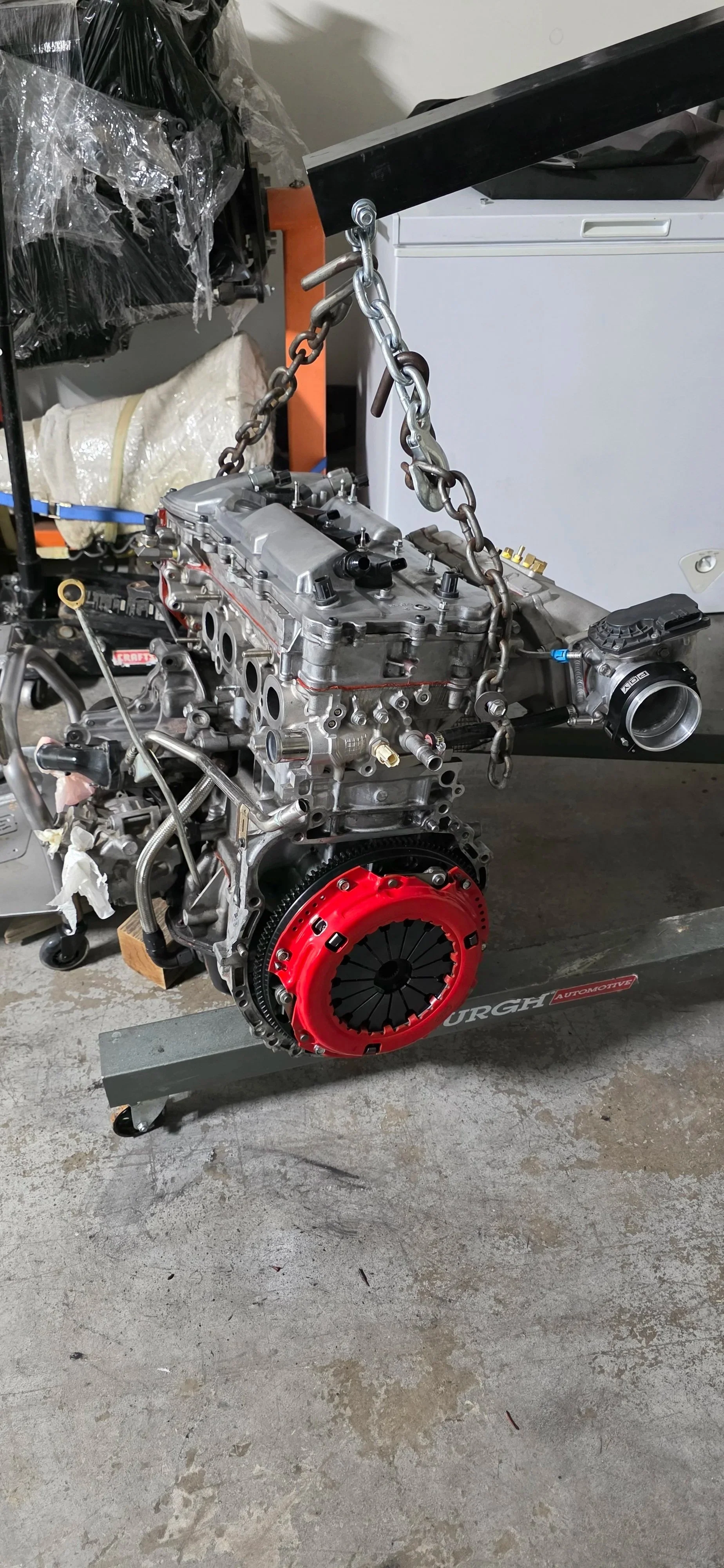 Car engine suspended by a chain hoist in a garage.