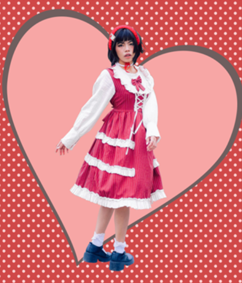 A young woman dressed in a pink and white layered dress with a white blouse, standing inside a heart-shaped outline against a red polka dot background with a pink center.