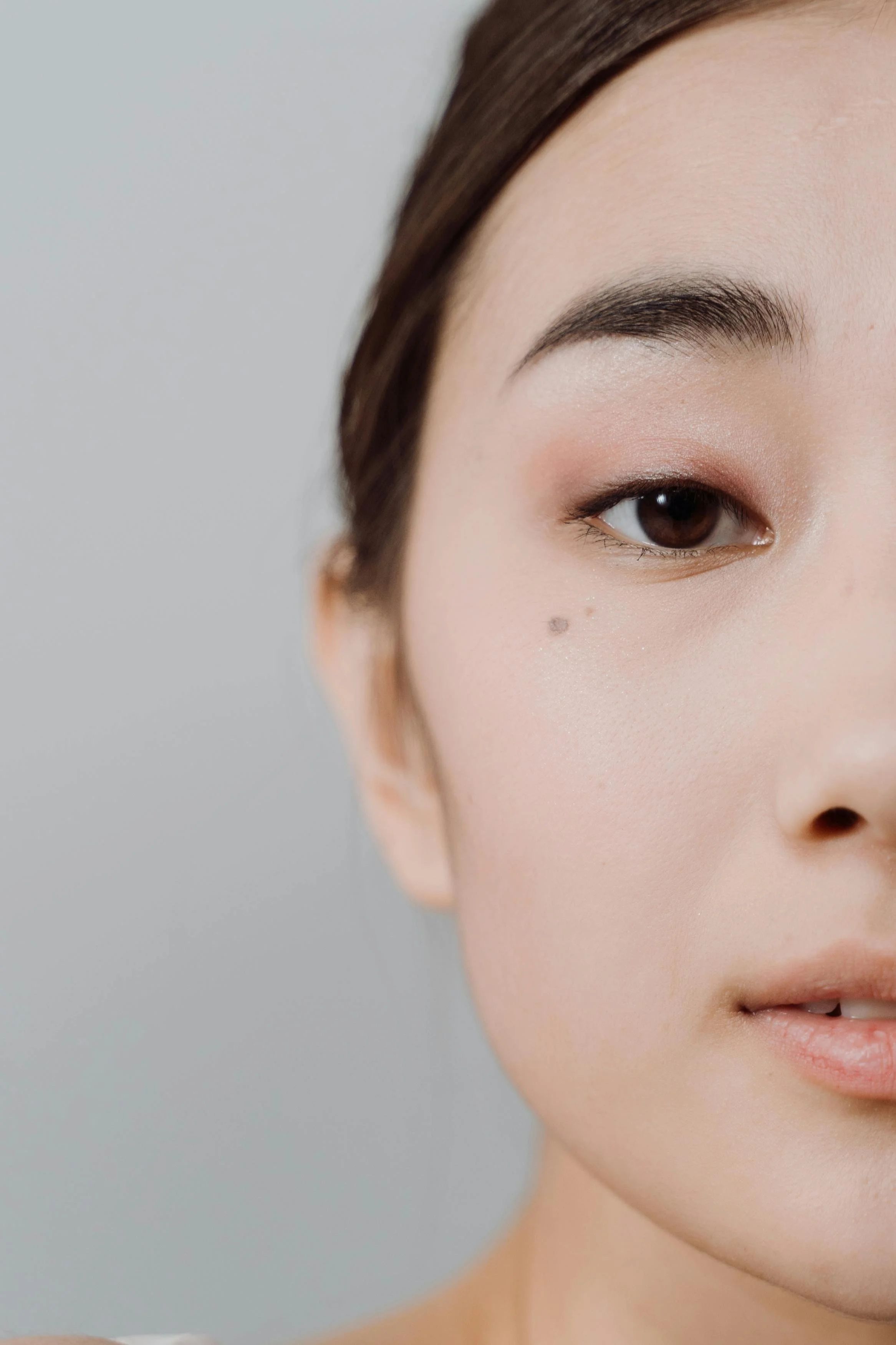Close-up of a woman's face showing her eye, eyebrow, part of her cheek, and lip, with smooth skin and natural makeup.