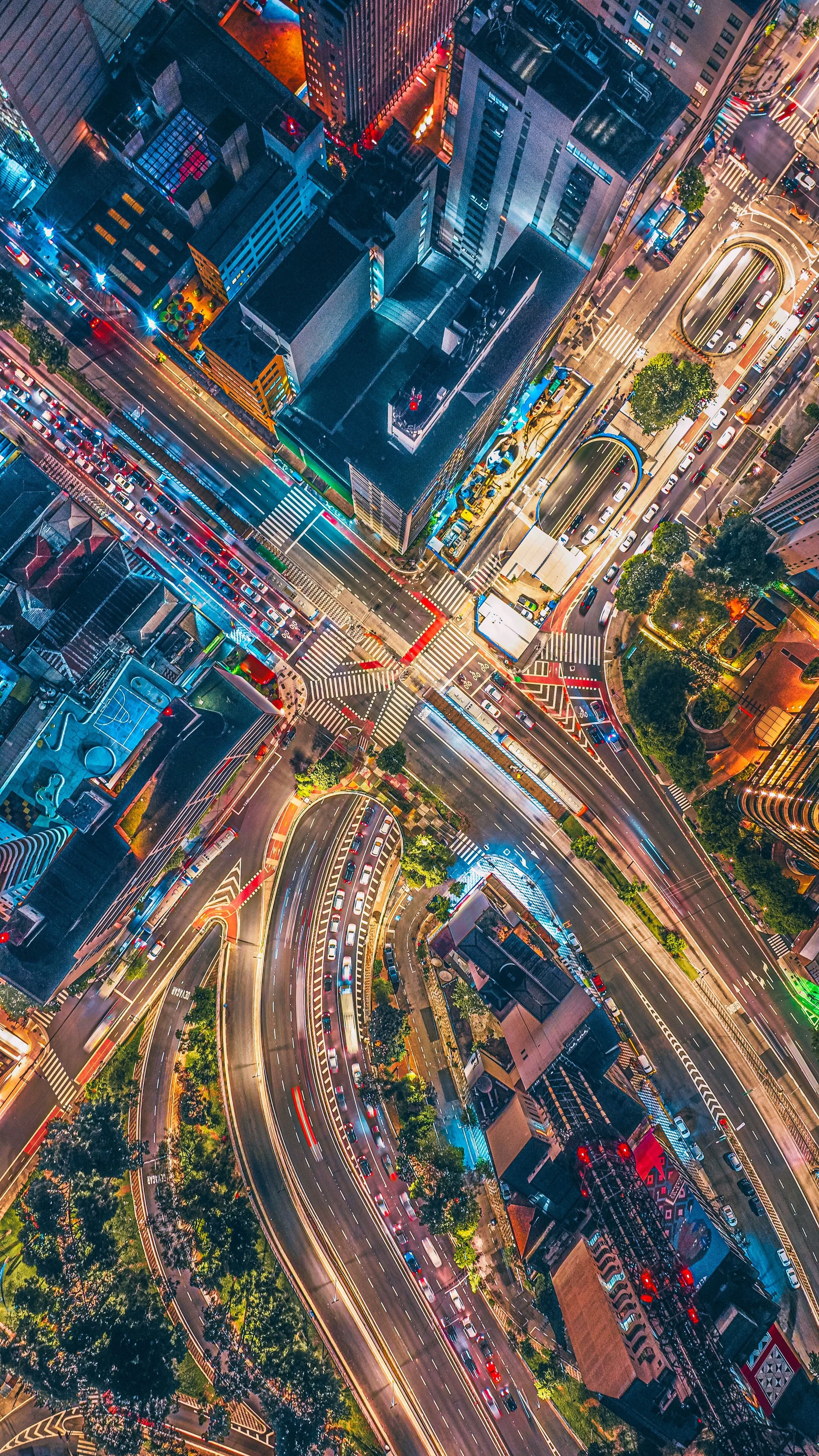 Bird's-eye view of a busy city intersection at night with illuminated streets, high-rise buildings, and moving cars creating light streaks.