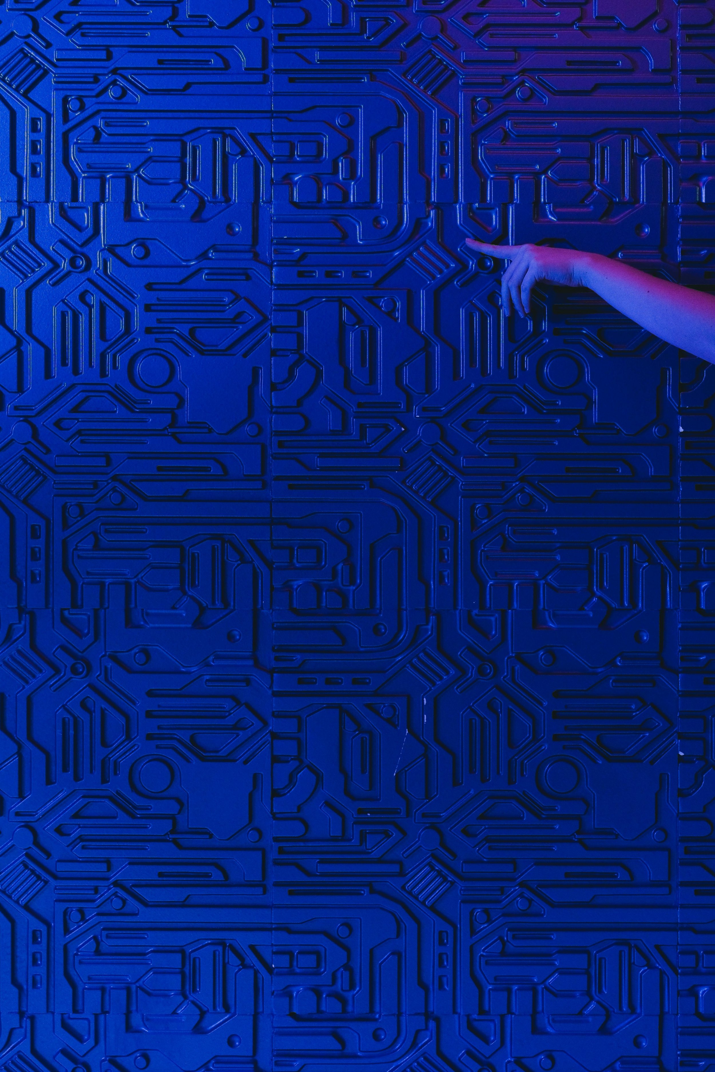 A hand pointing at a blue wall with a circuit board pattern design.
