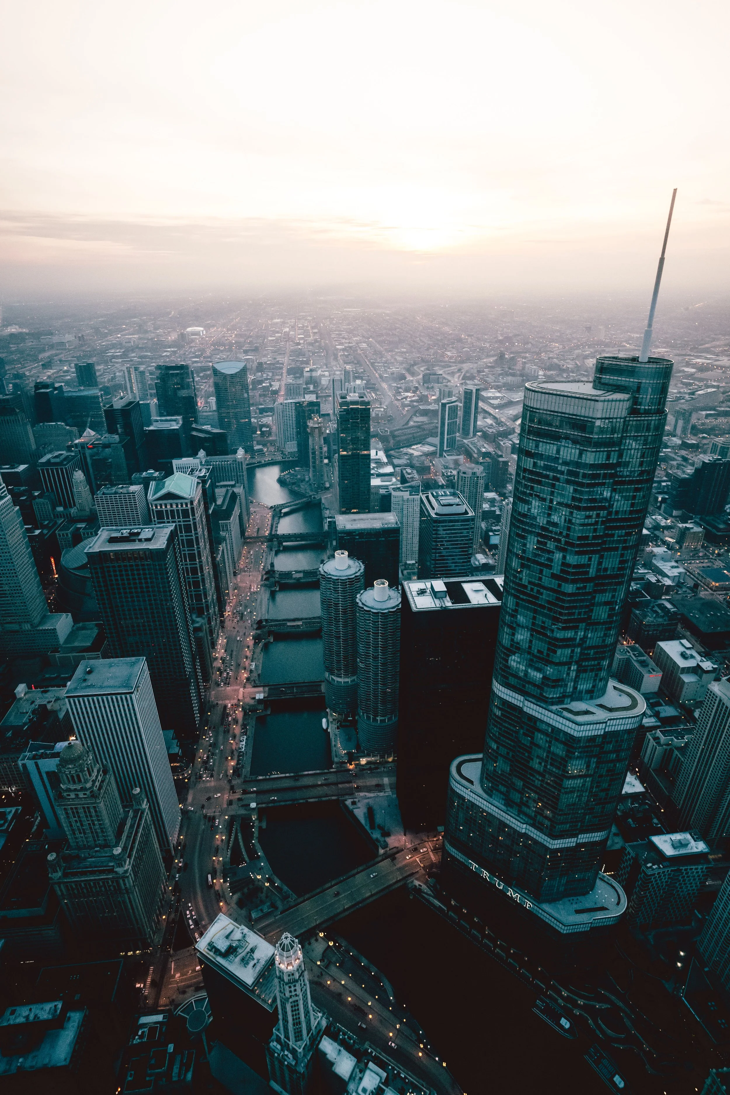 A city skyline at dusk with tall buildings, a river, and streets illuminated by streetlights.