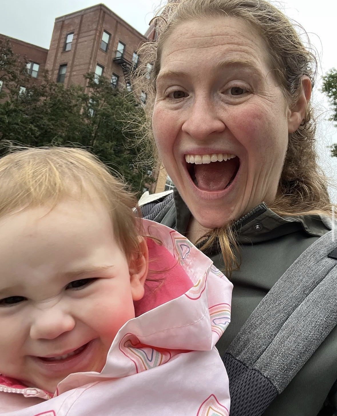 A woman and a young girl smiling and laughing together outdoors, with a building and trees in the background. Gut health specialist.