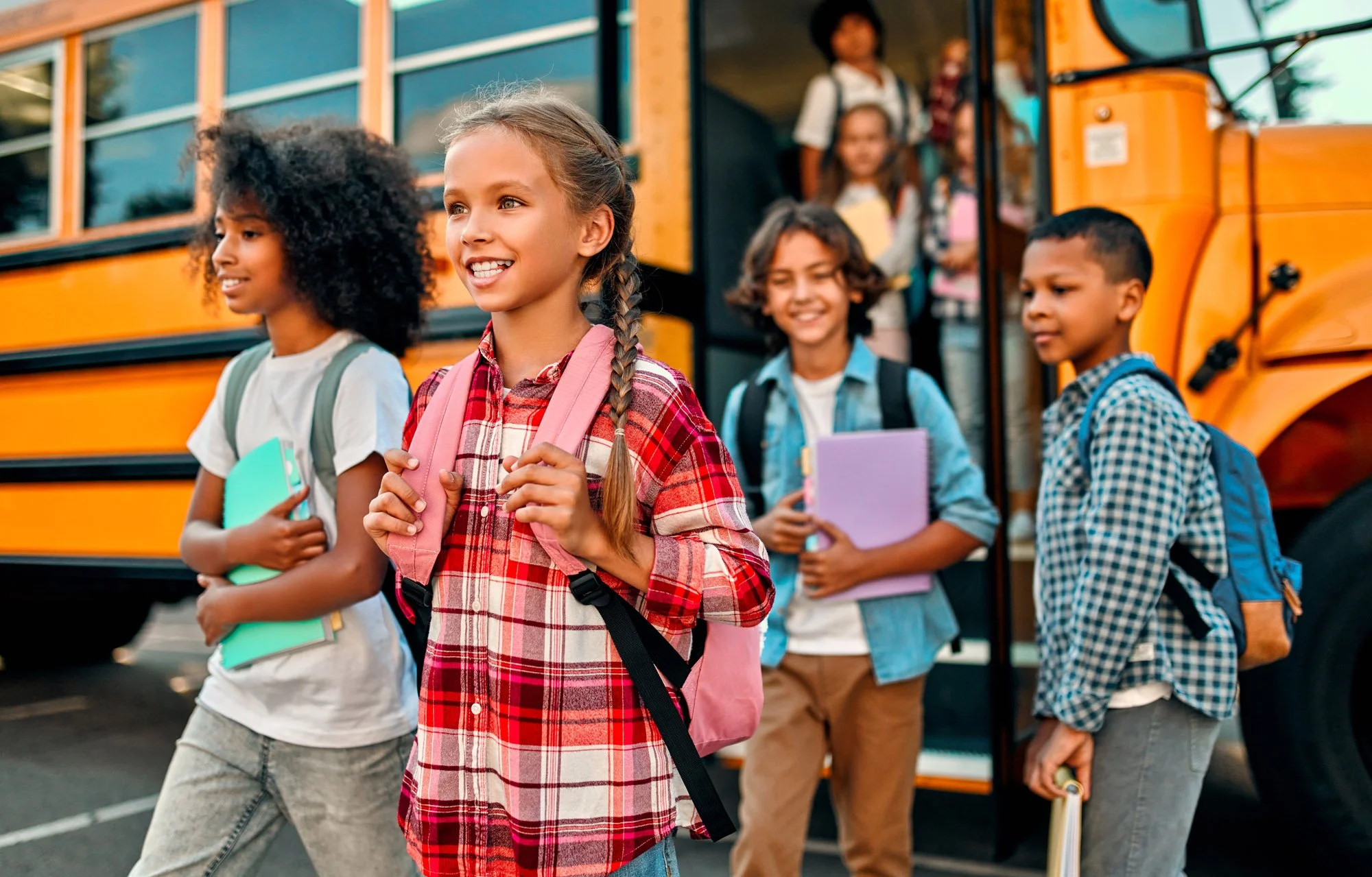 Group of young students disembarking from a yellow school bus, carrying backpacks and notebooks, outdoors during daytime.