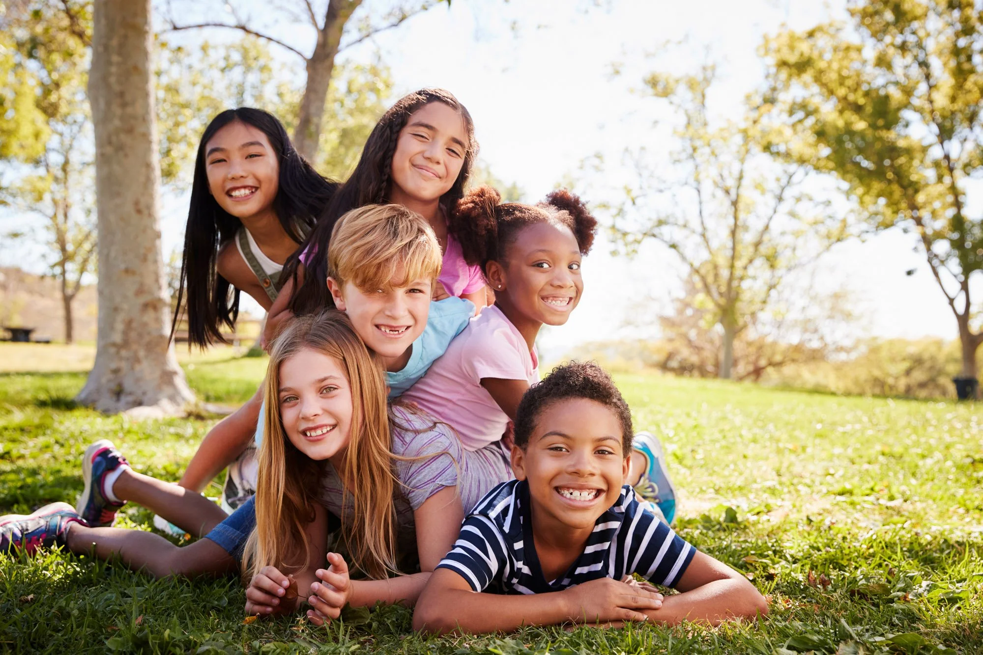 un grupo de niños sonrientes que forman una pirámide humana en un parque bañado por el sol