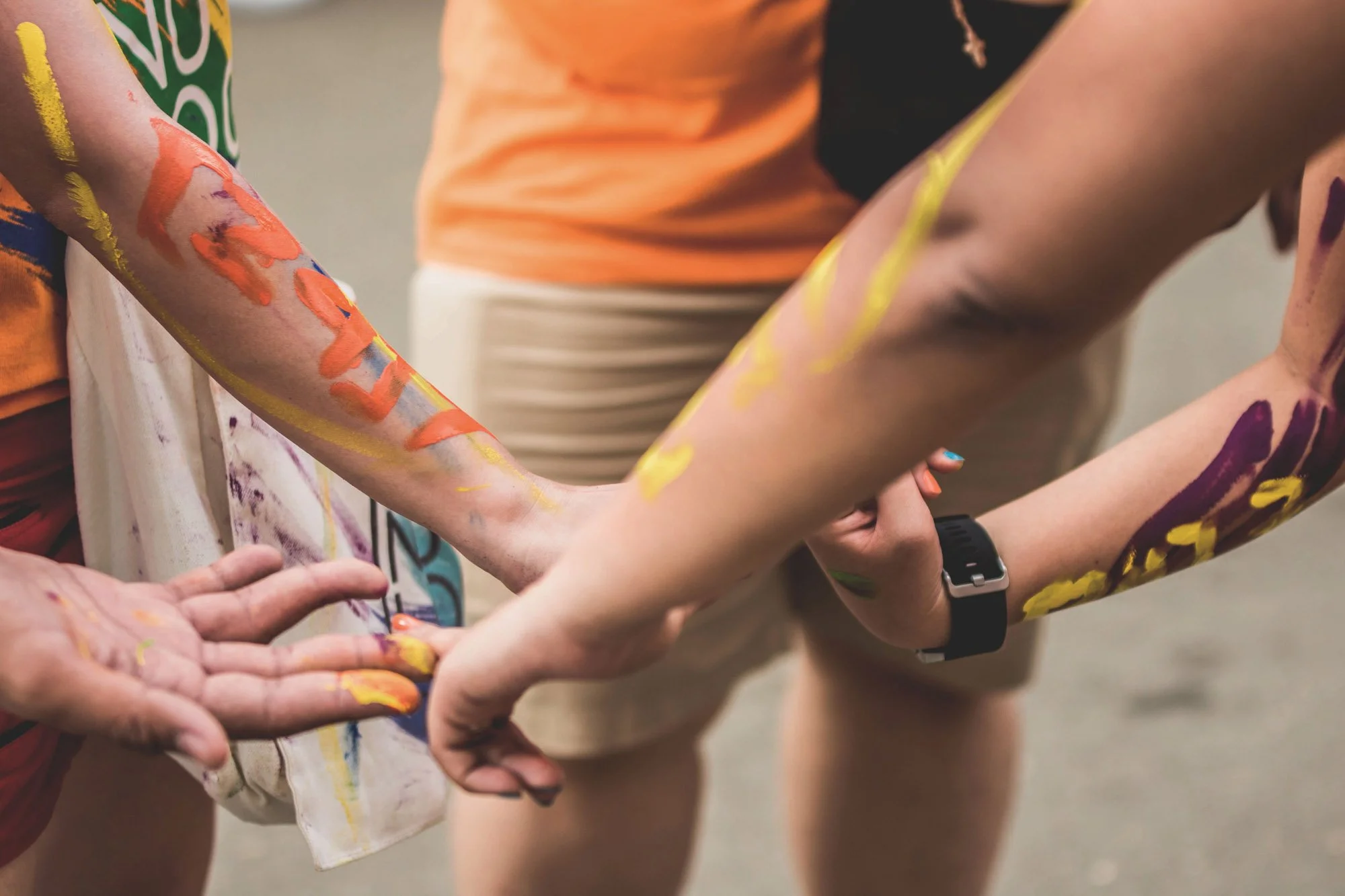 Personas con los brazos y las piernas pintados participando en una actividad en grupo, posiblemente relacionada con la pintura o el arte corporal.