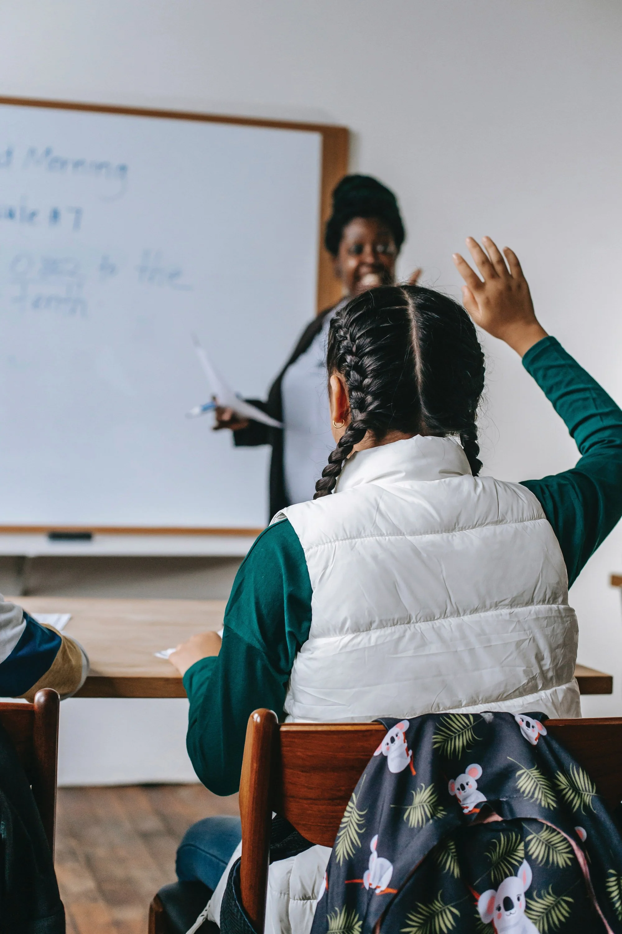 Un profesor llama a una alumna de secundaria que tiene la mano levantada en el aula.