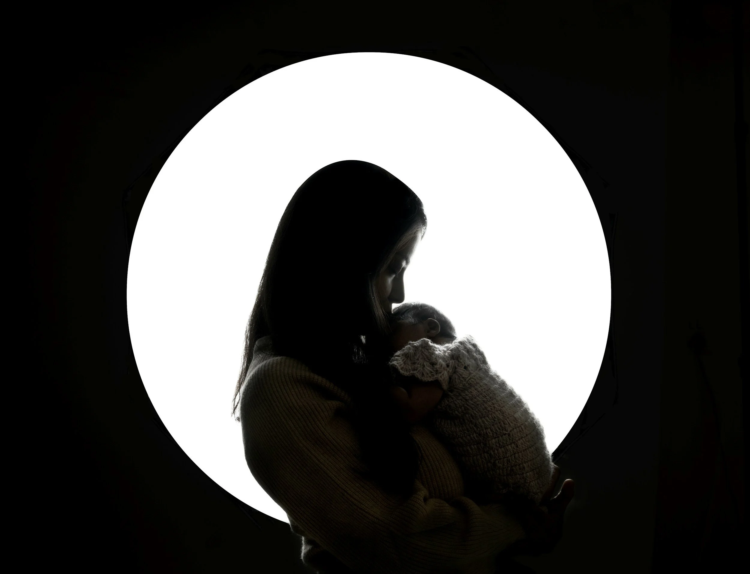 Silhouette of a woman holding a baby, with a bright circular background creating a halo effect.