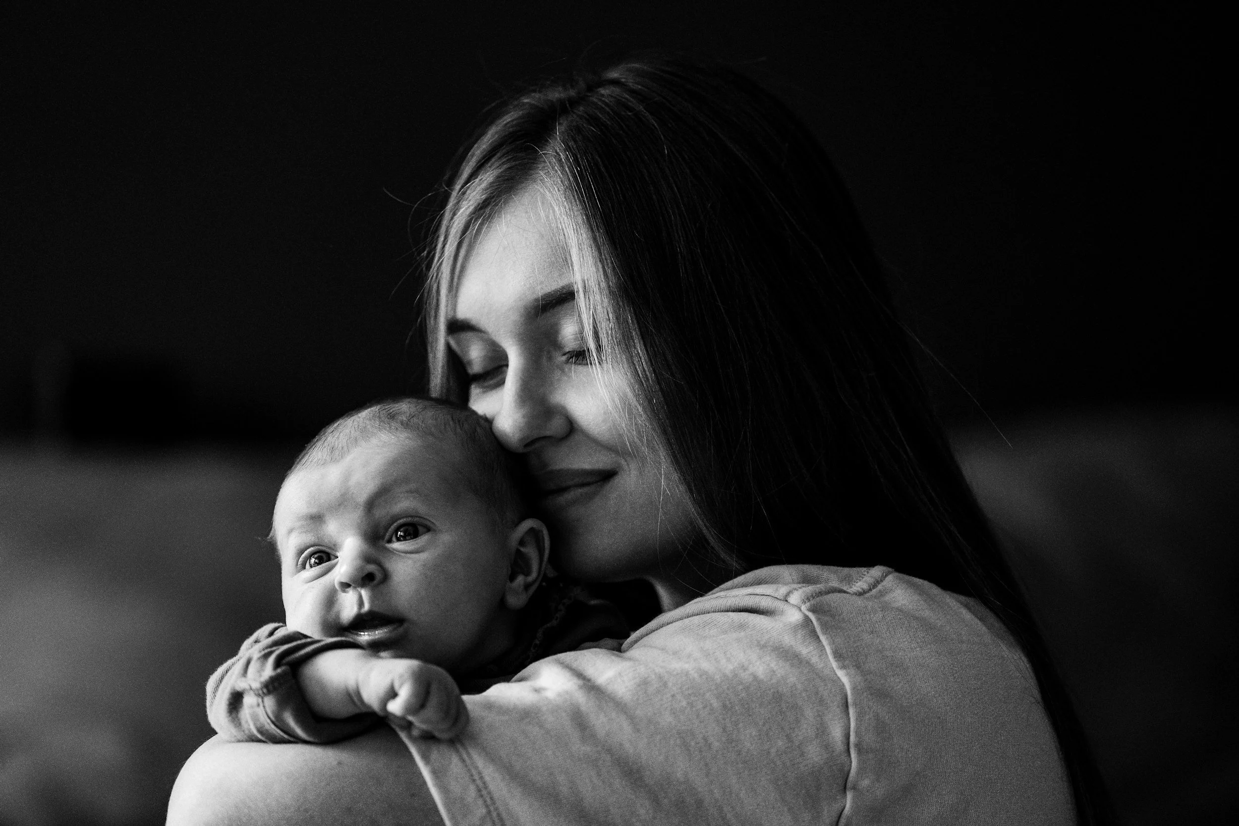 A woman holding a baby, both with eyes closed and gentle smiles, in black and white.