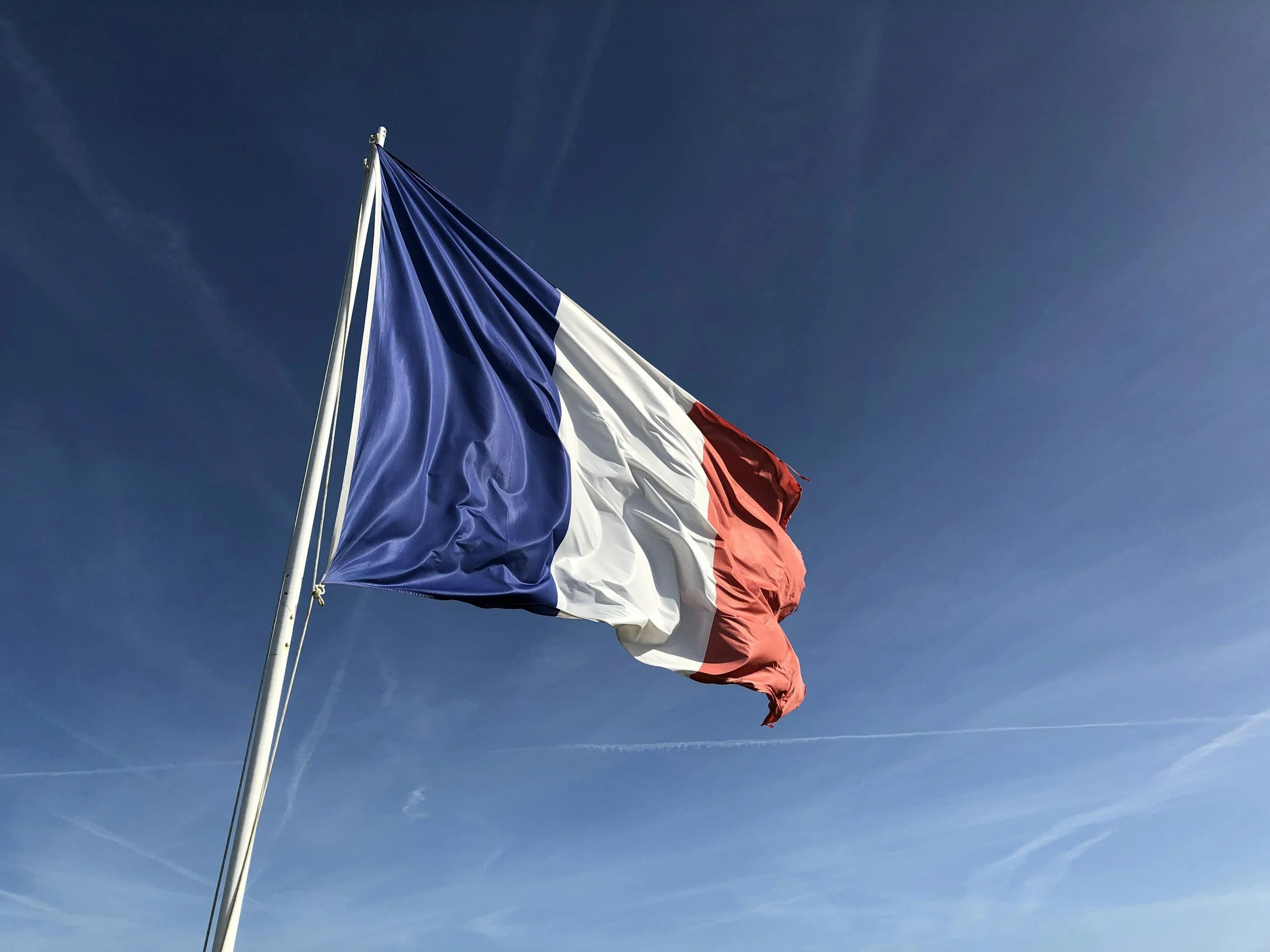 The French flag flying in the wind against a bright blue sky.