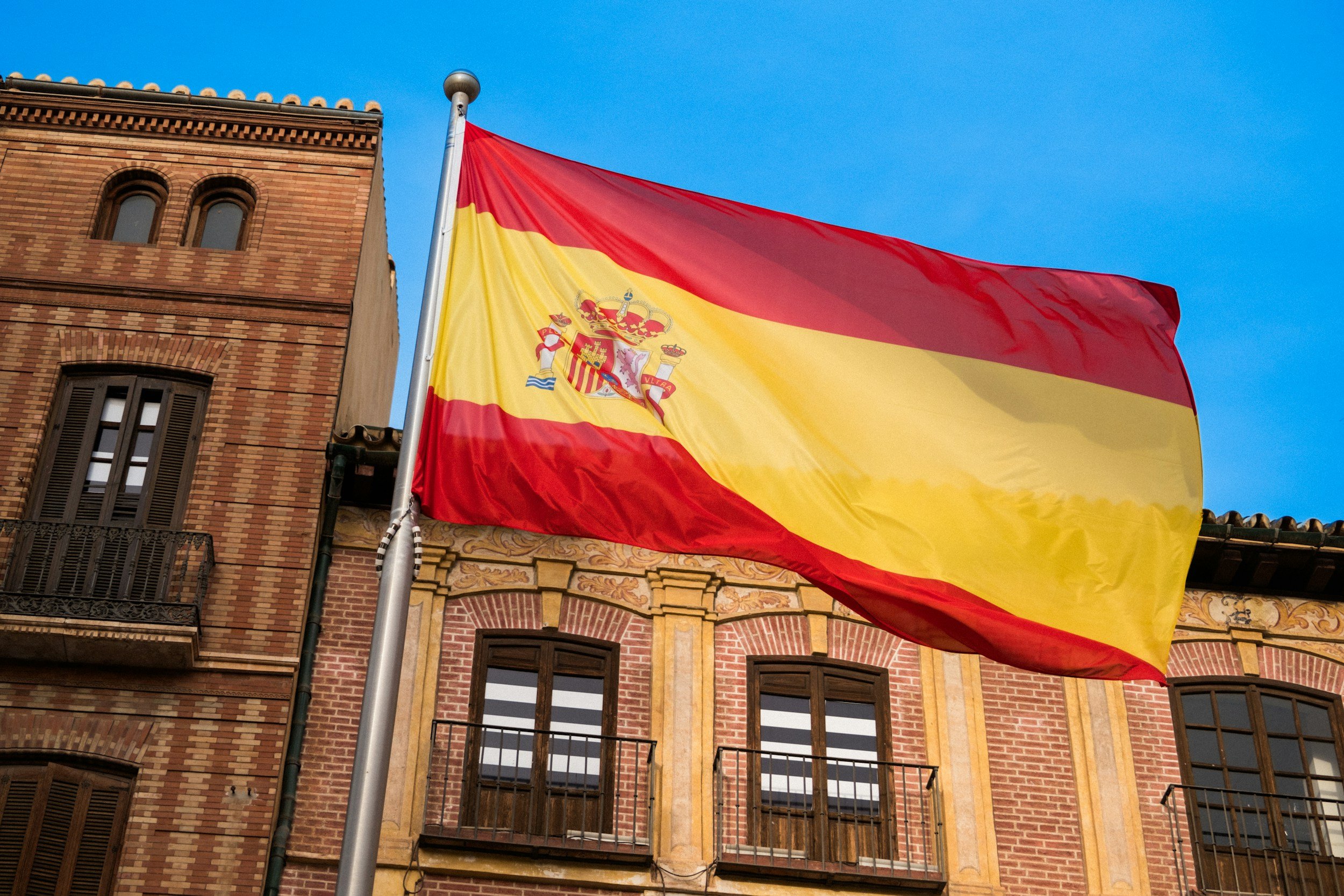 Spanish flag flying outside a brick building against a blue sky.