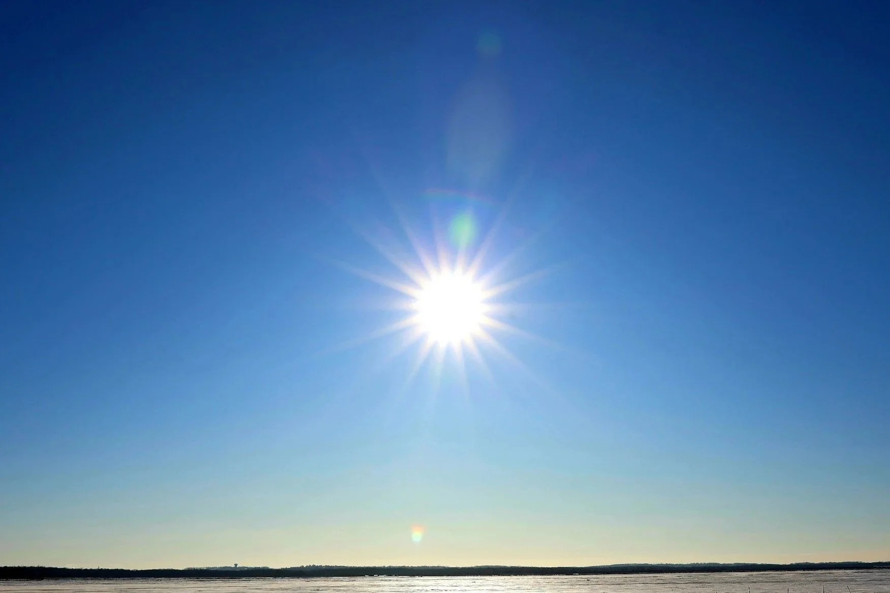 Bright sun in a clear blue sky over a flat landscape