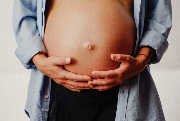 Person holding their pregnant belly with both hands, wearing a blue shirt and black pants