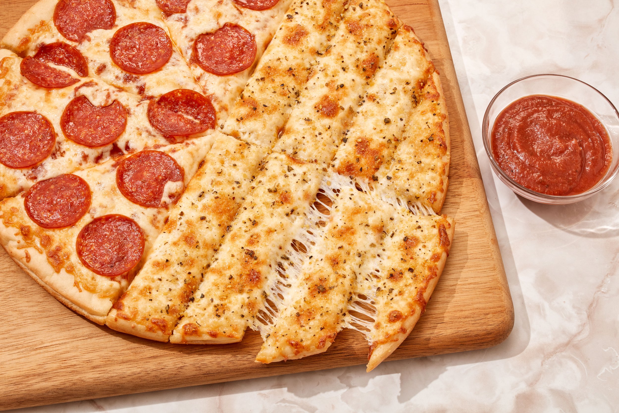 Pepperoni and cheese pizza on a wooden cutting board with a side of marinara sauce