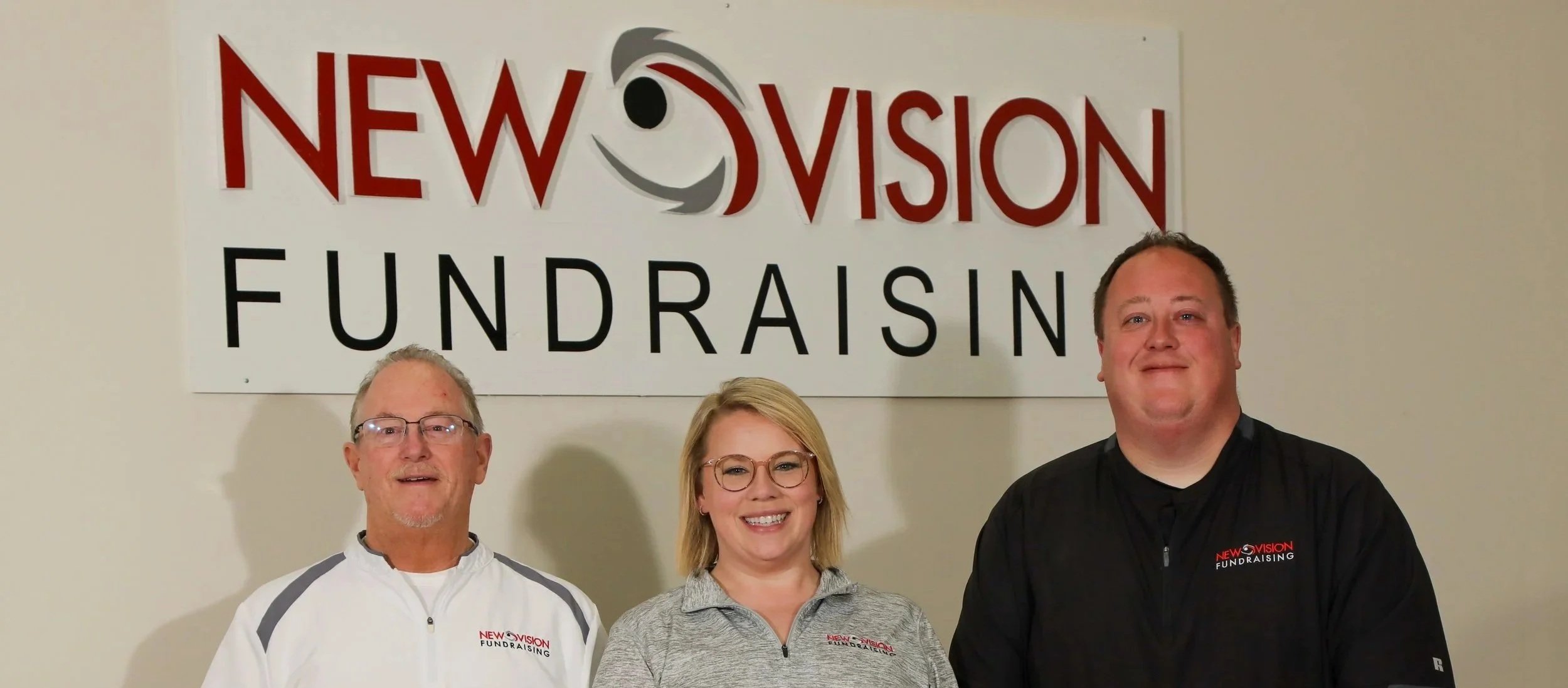 Three people standing in front of a sign that says 'New Vision Fundraising,' smiling at the camera.
