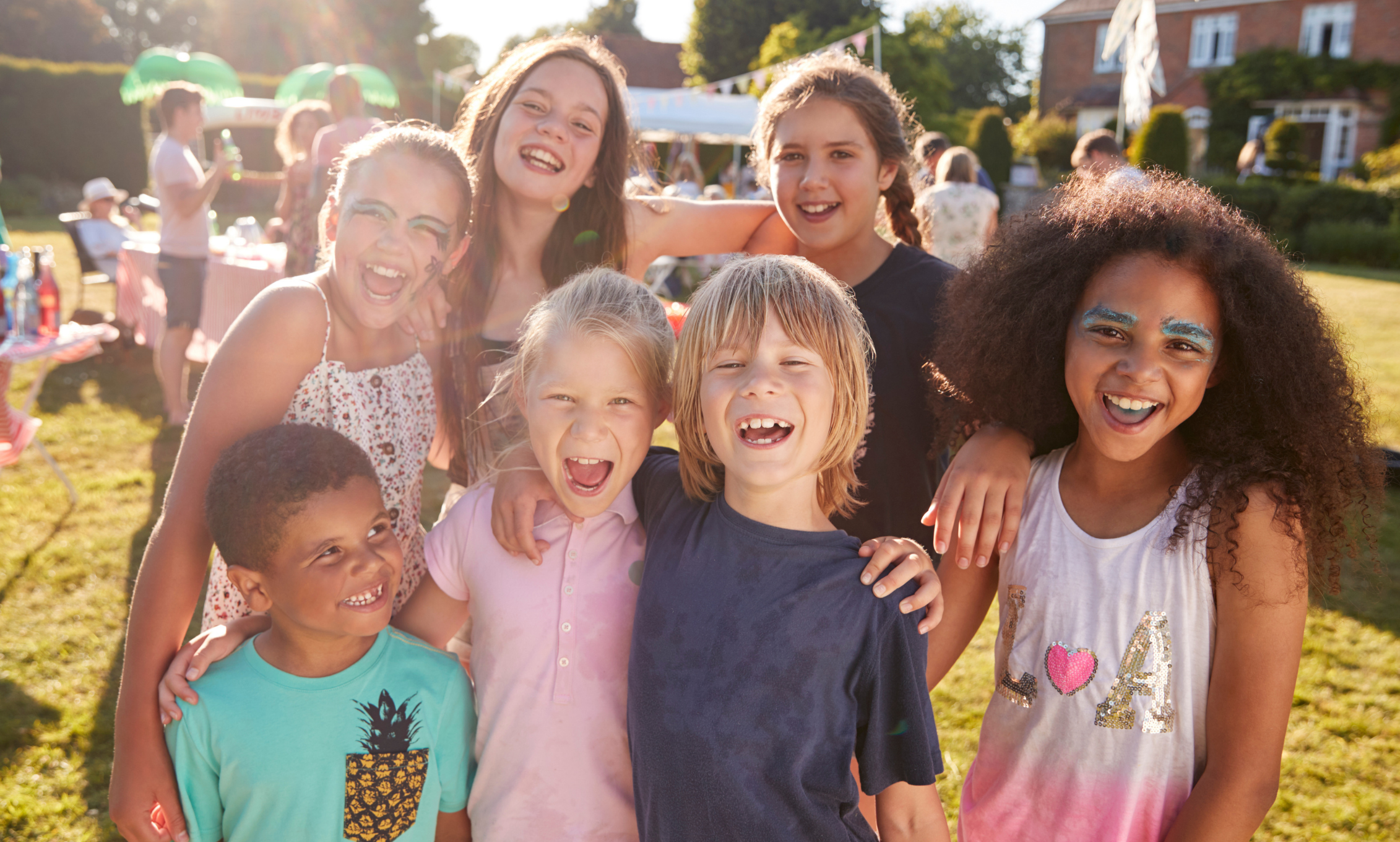 A group of children smiling and laughing outdoors at a sunny backyard gathering.