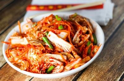 A bowl of kimchi with chopped green onions, placed on a wooden surface.