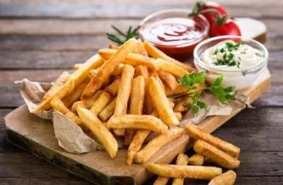 A serving of French fries with ketchup, mayonnaise, and fresh parsley on a wooden surface.