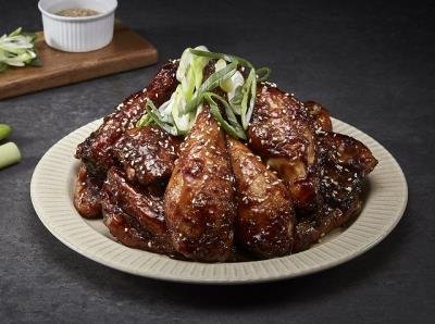 Plate of glazed glazed pork ribs garnished with green onions on a white plate, with a small bowl of dipping sauce and green onions in the background.