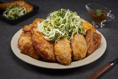 Fried chicken pieces topped with shredded cabbage and scallions, served with dipping sauce and a side of noodles.