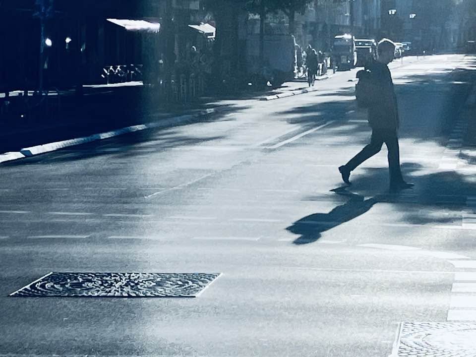 Ein Mann läuft bei Sonnenlicht über eine Straßenkreuzung, dessen Schatten auf die Straße fällt.