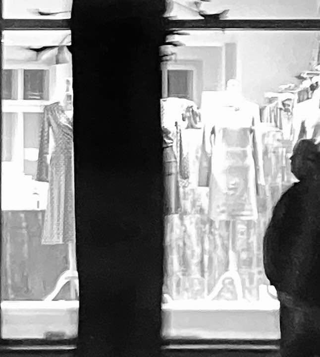 Schwarze Silhouette einer Person vor einem Schaufenster mit Kleidung auf Bügel im Stadtbild
