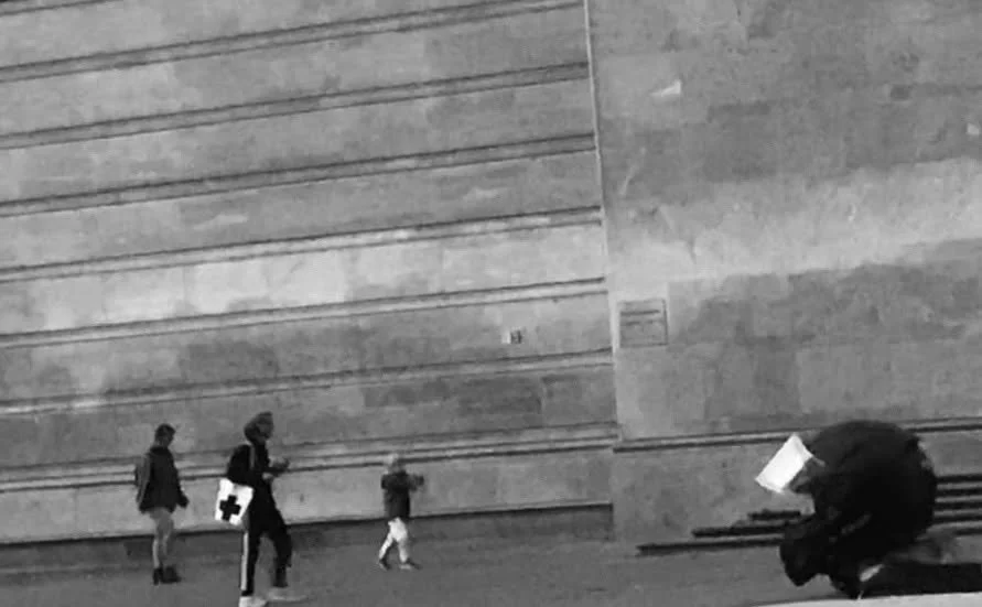 Gruppen von Menschen, darunter Kinder, die draußen vor einer großen Wand gehen, mit einer Person, die einen medizinischen Erste-Hilfe-Koffer trägt.