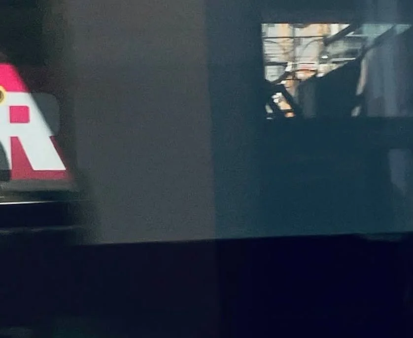 Teil eines Gebäudes mit reflektierten Fenstern und einem Fahrzeug im Hintergrund, das ist nicht klar erkennbar.