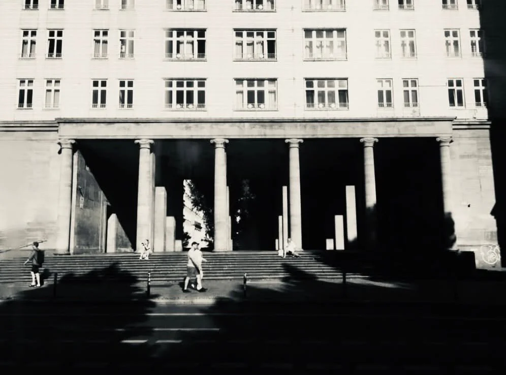 Schwarz-Weiß-Foto eines Gebäudes mit mehreren Fenstern und einer Säulenreihe an der Eingangstreppe, mit einigen Personen, die die Stufen entlang gehen.