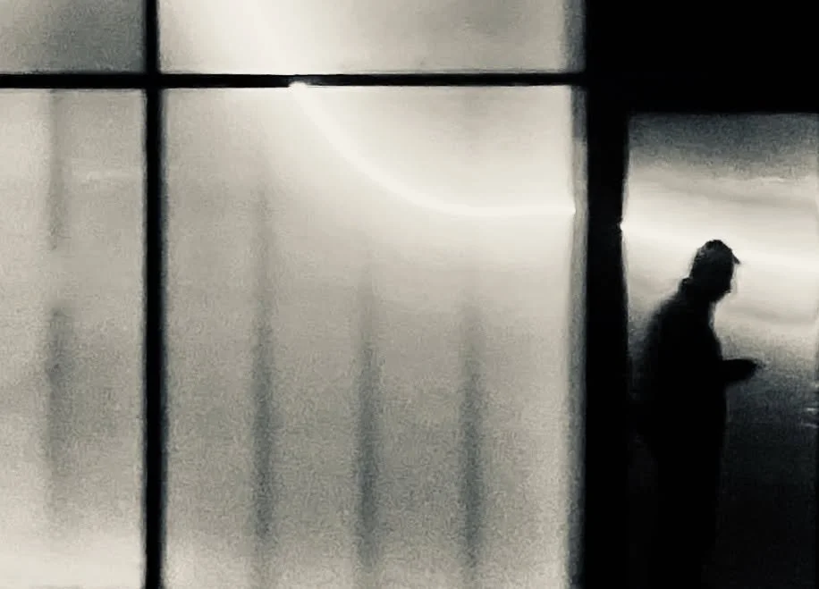 Silhouette einer Person, die durch ein Fenster blickt, in Schwarz-Weiß aufgenommen.