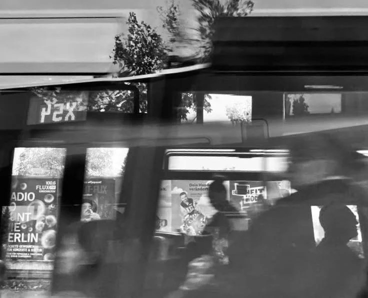 Dunkle Straßenbahn in Bewegung, reflektierende Werbeplakate an den Fenstern, Menschen im Inneren, bunte Werbetafeln auf der Bahn