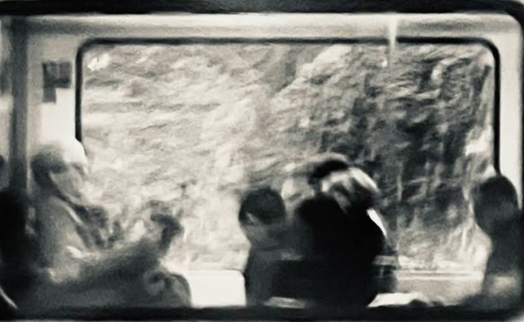 Schwarz-weiß-Foto von sechs Menschen, die in einem Zug sitzen und aus dem Fenster schauen.