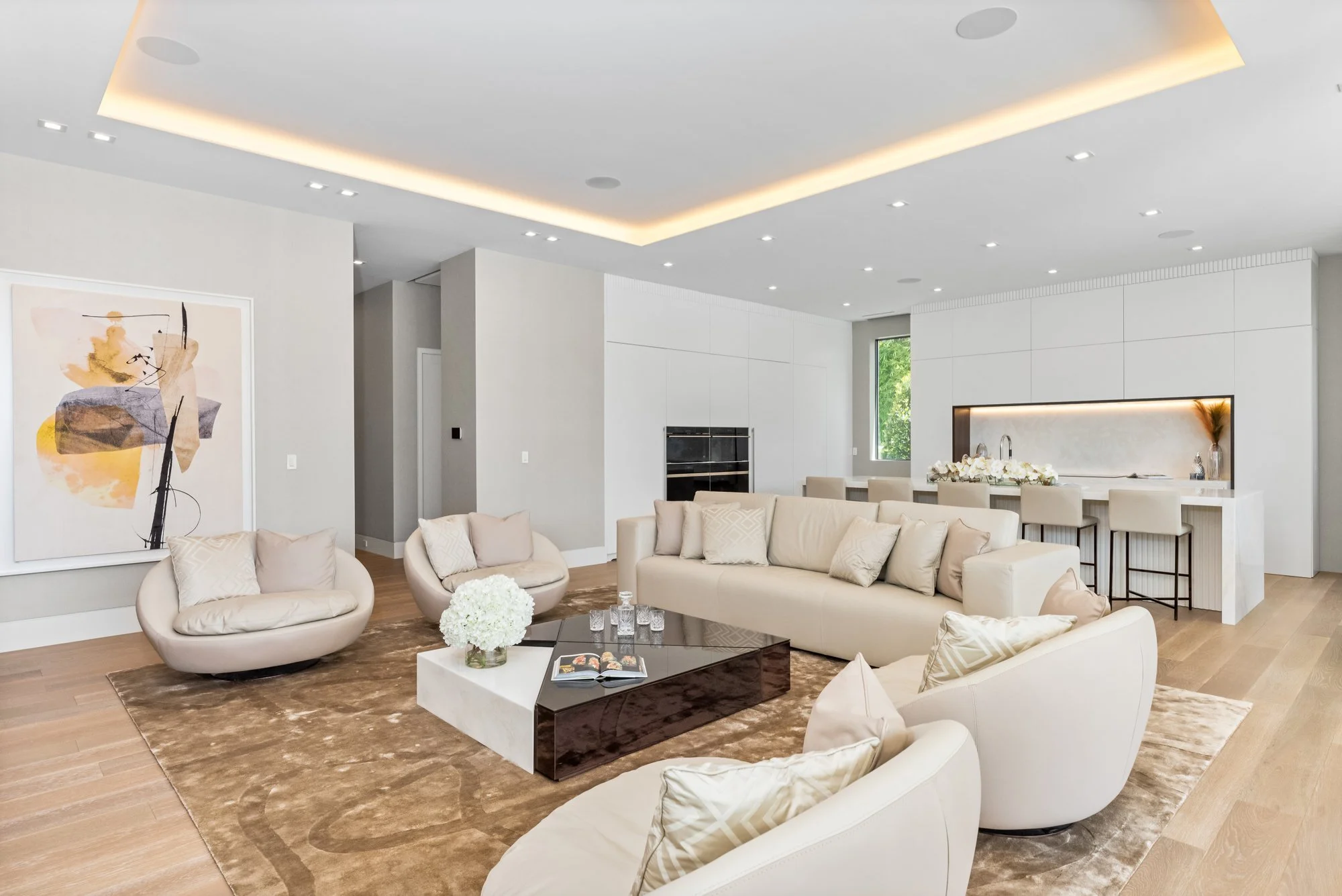 Modern, minimalist living room with white sofas, beige armchairs, a brown and white coffee table, and artwork on the wall.