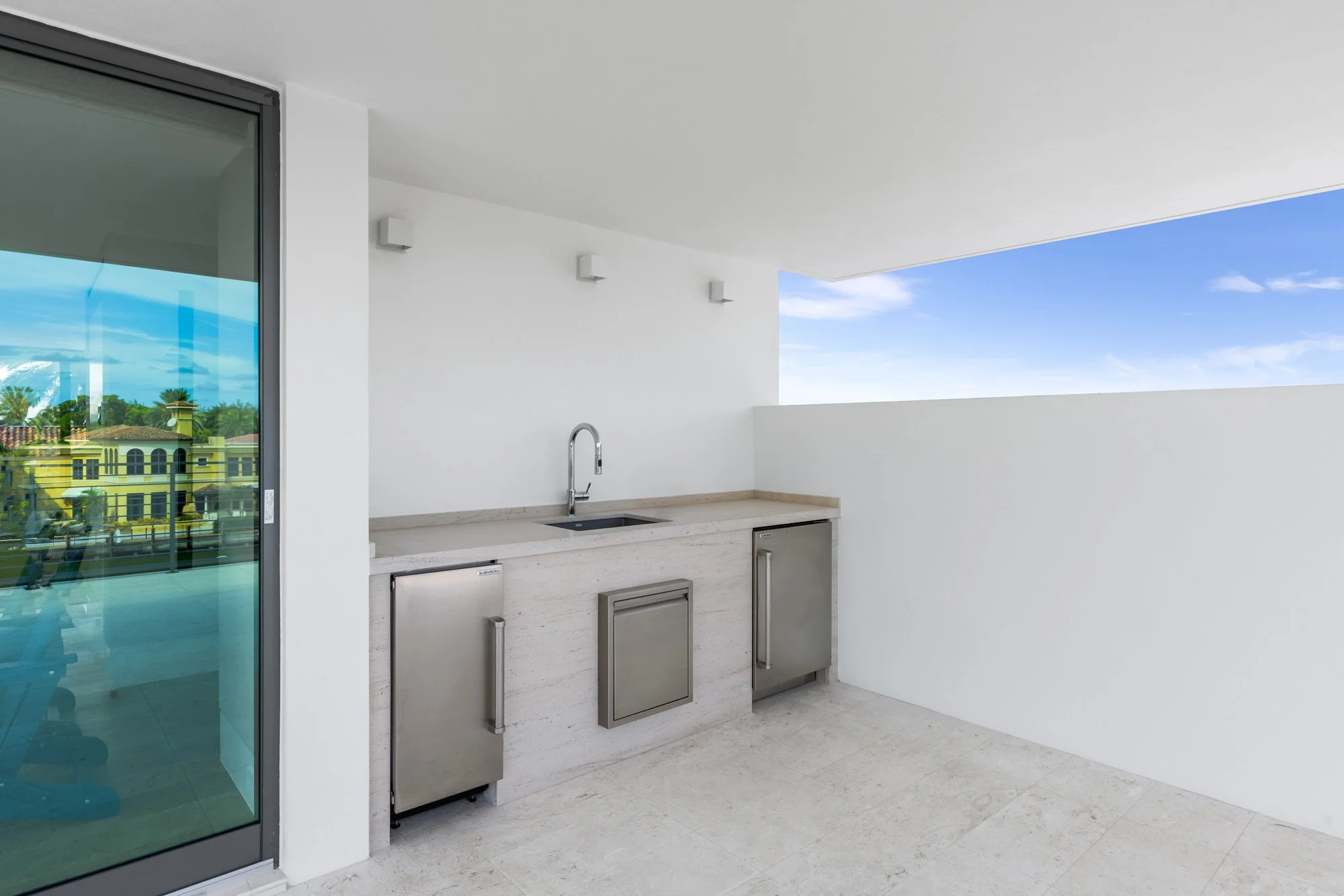 Outdoor balcony area with a small stainless steel kitchenette and a sliding glass door.