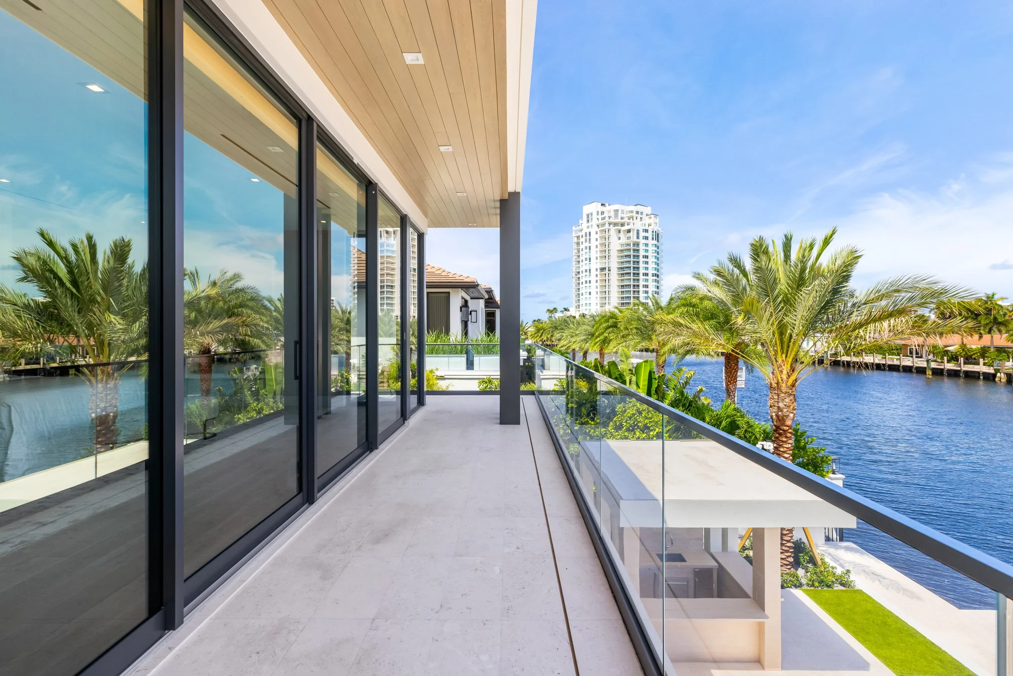 Balcony with glass railing overlooking water, palm trees, and high-rise buildings in the distance.