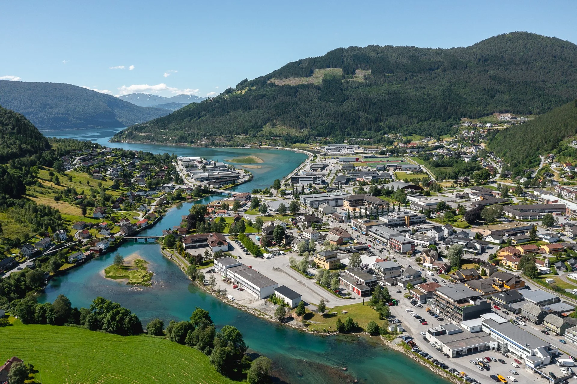 Sølvbyen i Norheimsund, med elva som renner gjennom sentrum, omgitt av grønne åser og fjell i bakgrunnen.