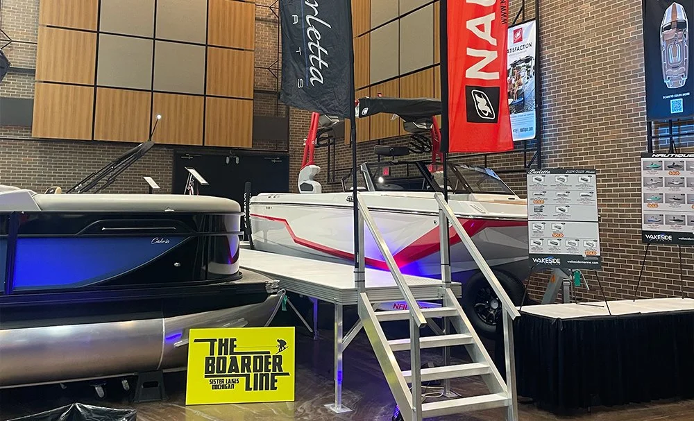 A display of boats inside a building, with one on a raised platform and another on the floor, along with informational panels and banners.