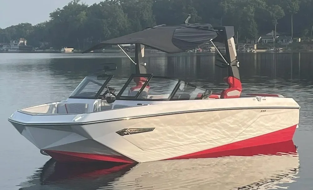 A white and red motorboat on calm water with trees and houses in the background.