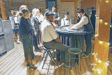People in vintage attire gather at lively fundraising casino events, enjoying festive vibes under string lights on wooden floors.