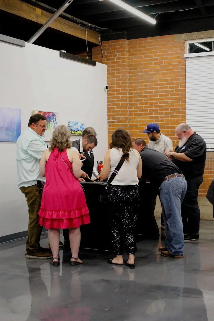 A group of people standing and looking over a casino game table with artwork in the background.